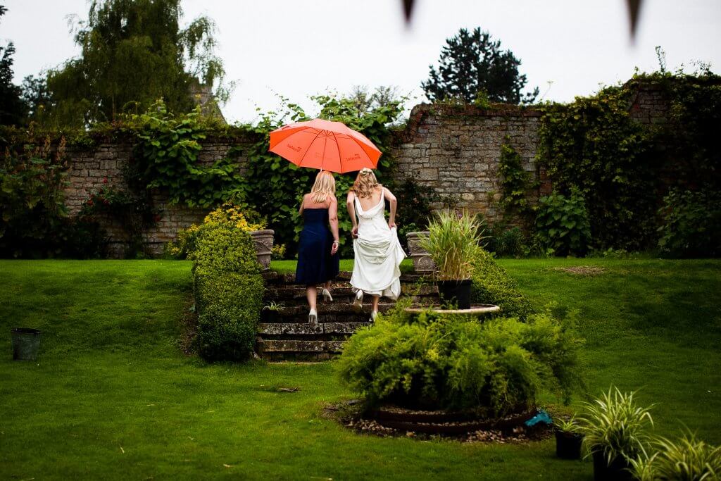 Bride with bridesmaid under umbrella in garden