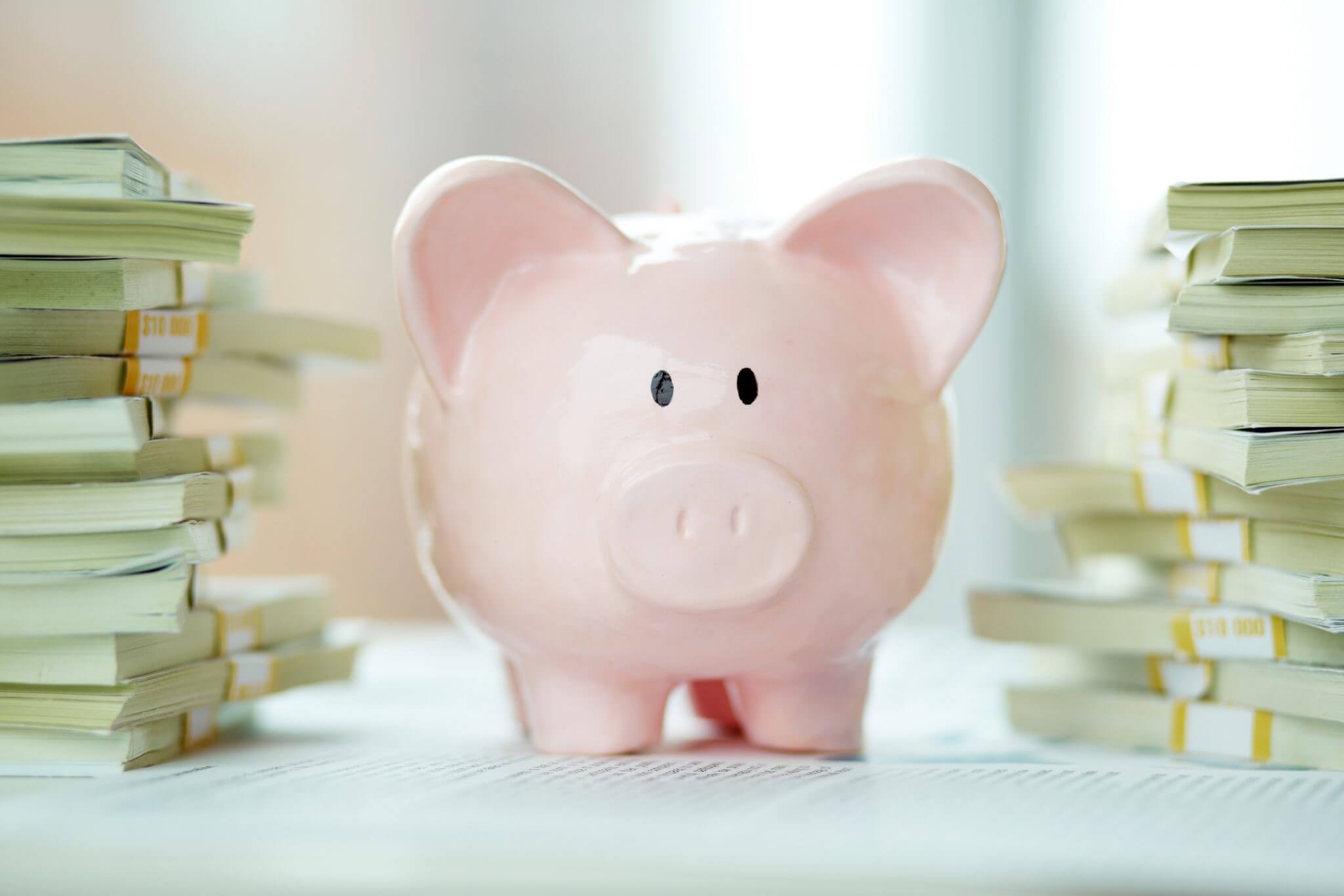 Image of pink piggy bank surrounded by stacks of dollar bills - guide to saving for your children